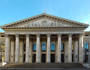 Obraz premium Munich National Theatre’s neoclassical facade with grand Corinthian columns and sculptural pediment, golden hour light, symmetry and cultural significance