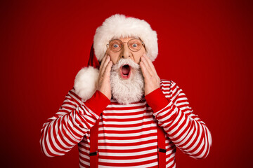 Surprised Santa in red striped shirt with suspenders and hat against bold red background for...