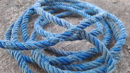 Close-up of a sturdy, weathered blue rope coiled and tangled on a rough gray concrete surface, showing texture and detail.