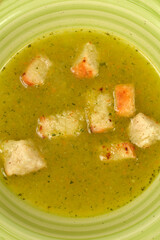 A close-up, vertical shot of a vibrant, creamy green zucchini and carrot soup, garnished with golden-brown croutons in a light green bowl