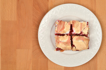 Four square pieces of meringue-topped redcurrant cake are presented on a white decorative plate on a light wooden background