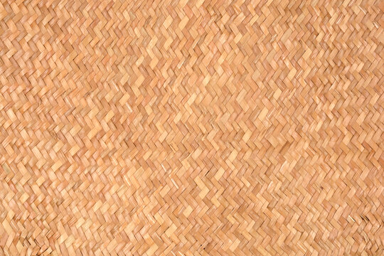 A full-frame close-up showcases the tight, herringbone or chevron pattern of a natural light brown woven mat or basket texture