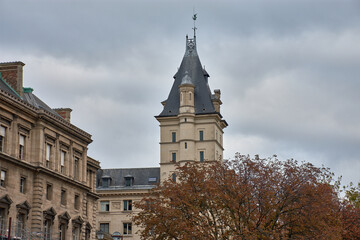 Facade of the Palais de Justice in Paris seen from the Seine with a pointed tower and trees with autumn foliage