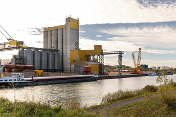 Large industrial facility silos cranes stands Mittellandkanal cargo ships docked loading operations. Calm water industrial equipment reflect economic activity and regional infrastructure development