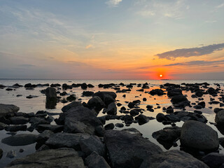 Beautiful sunset scene over a rocky shore. A stunning sunset paints the sky in fiery hues over rugged coastal rocks, with golden reflections on the water. Peaceful evening atmosphere.