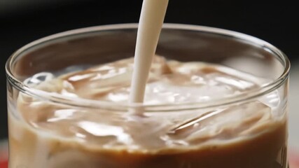 Closeup of fresh milk being poured into a glass of iced coffee creating a beautiful swirl of brown and white liquids perfect for a refreshing beverage advertisement or a cozy morning scene. - Powered by Adobe