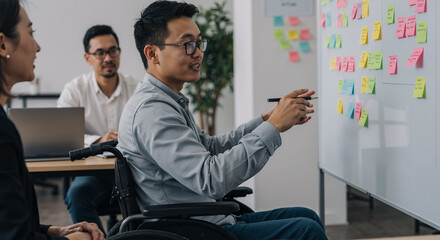 asian man in wheelchair leading team meeting with colleagues at modern office with sticky notes