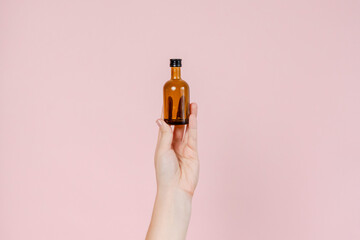 Small glass blank bottle mockup in hand on pink background. Package for cosmetics product,...