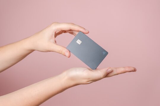 Close up elegant hand hold a blank credit card with online service for mockup isolated on pink background. Modern way of banking and buying