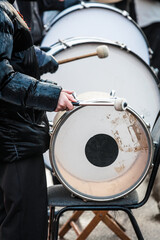 Drummer in black puffer jacket plays bass drum with mallets outdoors &mdash; close-up of hands, worn drum head, and winter performance energy perfect for music, culture or event themes.