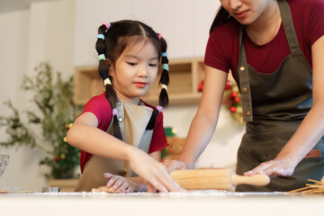 Baking Fun: Young girl rolling dough with mother in a festive kitchen