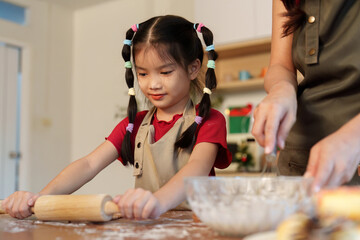 Baking Together. Young girl rolling dough with her mother in a festive kitchen.