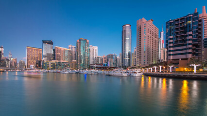 Fototapeta premium Dubai Marina towers and yachts reflected in water of canal in Dubai day to night timelapse