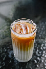 Iced coffee latte with layers of espresso, milk, and ice on a dark table, a refreshing and cool beverage