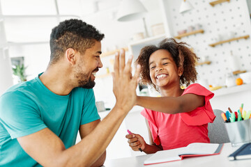 Father and daughter doing homework at home. Father and teenage daughter girl sitting at the table coloring and writing. Mother and daughter giving high five hand to each other. Teamwork and cooperatio