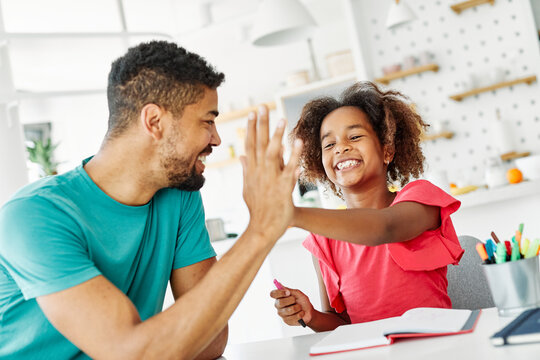 Father and daughter doing homework at home. Father and teenage daughter girl sitting at the table coloring and writing. Mother and daughter giving high five hand to each other. Teamwork and cooperatio