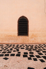 Minimal beige Moroccan wall with a black window and scattered black sheets of paper on the ground, evoking mystery and simplicity.