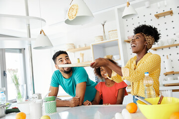 Mom and Dad, parents teaches daughter how to flip pancakes, prepare food,  in kitchen at home