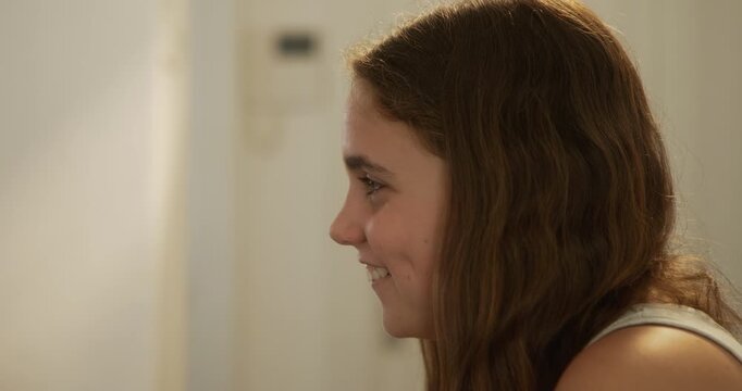 Profile shot of teenage sister smiling at teenage brother playing cards in their living room. 