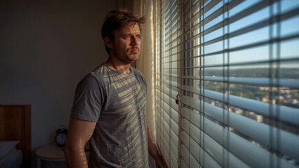 Morning light streaming onto man shifting gaze to view cityscape by bedroom blinds, holding cord - Powered by Adobe