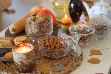 Lit candles, cookies, chocolate, nuts, tea, wine, pumpkins, books, reading glasses and autumn leaves on the table. Autumnal hygge at home. Selective focus.