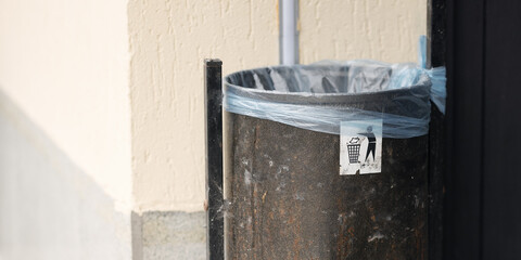 Urban trash bin with blue plastic bag and litter symbol on city street. Concept of cleanliness,...
