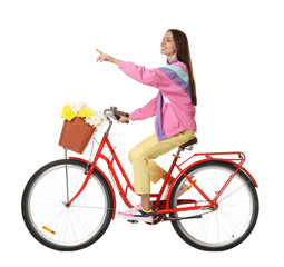 Smiling woman riding bicycle with basket of flowers and pointing at something on white background