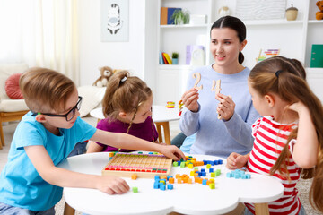 Fototapeta premium Cute children and smiling teacher at white table during lesson in elementary school
