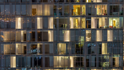 Windows of the multi-storey building of glass and steel lighting inside and moving people within timelapse
