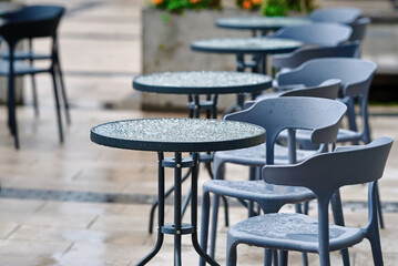 Empty restaurant terrace after rain, wet tables and chairs. Street terrace during rain in autumn season. Wet table with water droplets. Wet tables and chairs standing empty after rainfall