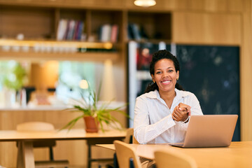 African-American Woman Working On Laptop In Modern Cafe, Smiling And Engaged In Work