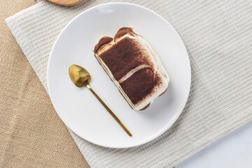 Tiramisu dessert on white plate with gold spoon