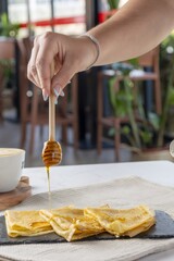 Hand pouring honey on crepes for breakfast