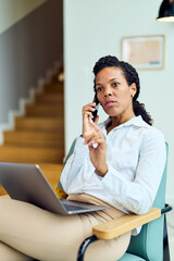 African-American Woman On Phone During Work Call With Laptop In Modern Office