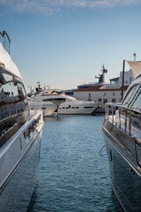 Between two luxurious yachts, a pristine white vessel rests gently in the calm marina waters, framed by reflections and bathed in soft evening light at Limassol Marina
