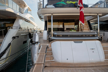 Luxury yacht stern with teak decking and stairs leading to upper levels. Polished metal railings and a comfortable seating area under a shaded canopy at Limassol Marina.