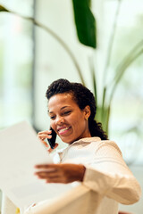 African-American Woman Smiling While On The Phone And Reviewing Documents In Office