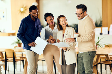 Diverse Team Reviews Documents And Discusses Ideas During Casual Office Meeting In Modern Workspace...