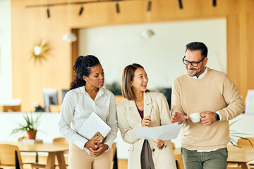 African-American Woman, Asian Woman, and Man Collaborate Over Documents in Modern Office