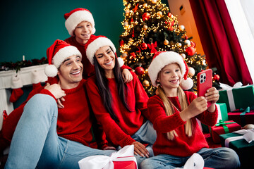 Happy family in red celebrating Christmas by a decorated tree with gifts