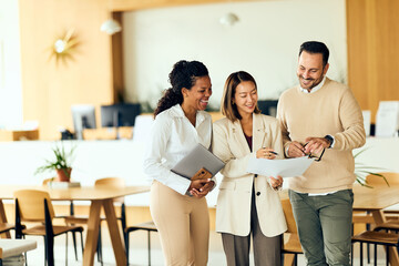 African-American Woman, Asian Woman, and Man Collaborate Over Documents in a Bright Modern Office