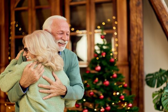 Joyful Elderly Couple Embracing Near Christmas Tree in Cozy Home Celebration