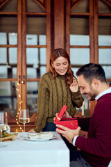 Couple Enjoys Gift Exchange at Festive New Year Dinner Setting by Windowed Wooden Doors