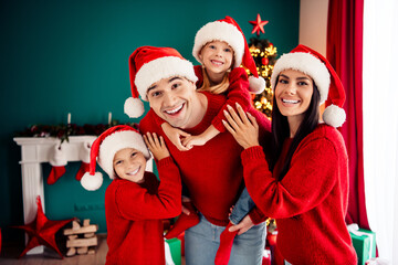 Happy family celebrating Christmas in cozy home with tree and decorations, wearing red sweaters and...
