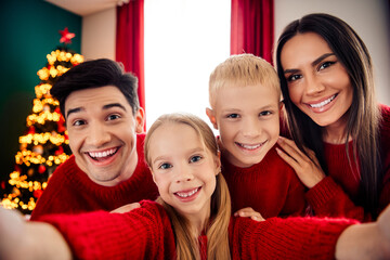 Happy family dressed in red enjoying Christmas together at home with a festive decorated tree in...