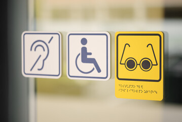 Accessibility symbols on glass door showing support for people with disabilities — hearing, wheelchair, and vision assistance. Concept of inclusivity and public accessibility. Editorial use only.