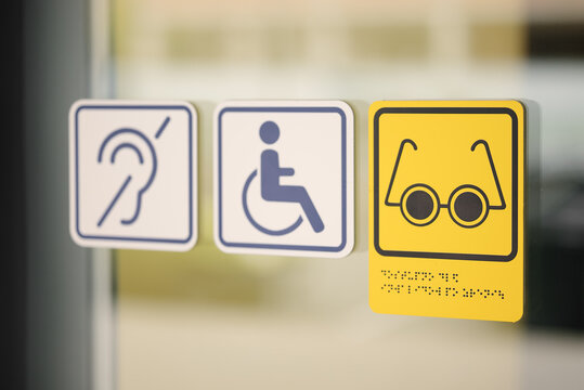 Accessibility symbols on glass door showing support for people with disabilities — hearing, wheelchair, and vision assistance. Concept of inclusivity and public accessibility. Editorial use only.