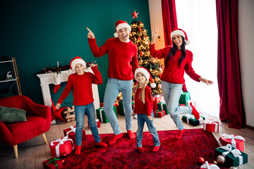 Festive family in red sweaters celebrating Christmas near decorated tree with gifts, enjoying...