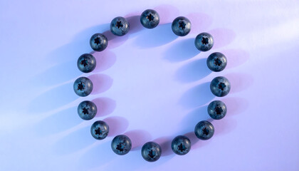 A circle of fresh blueberries arranged on a light purple surface, with blue and white light creating soft shadows.