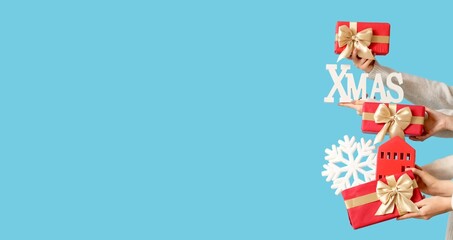 Hands holding gift boxes and Christmas decorations on blue background with space for text